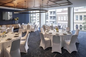 A modern dining area with round tables, white chairs, and a large window offering a city view. - Voco Auckland City Centre (Auckland)
