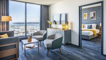 Quarto de hotel com uma janela grande, uma mesa, duas cadeiras, uma cama e um espelho.