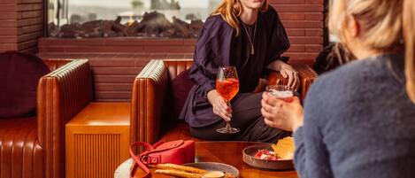 A person sitting on a leather couch with a glass of drink, a red bag, and a plate of food on a table.