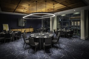 A conference room with a round table, black chairs, a wooden ceiling, and a modern light fixture. - Voco Auckland City Centre (Auckland)