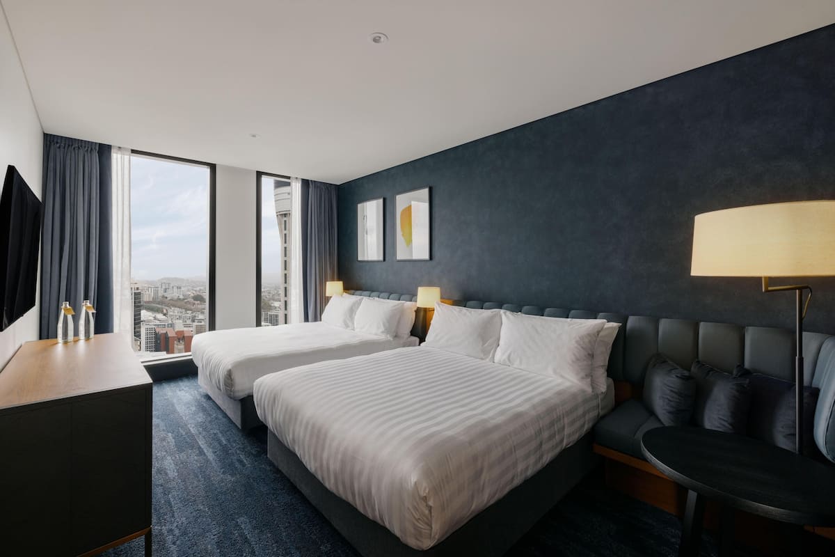 A hotel room with two beds, a desk, a sofa, and a view of the city.