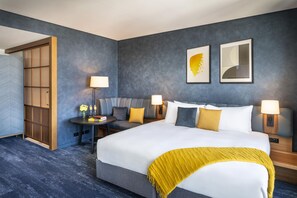 A hotel room with a large bed, two bedside tables with lamps, a sofa, and a wooden wardrobe. - Voco Auckland City Centre (Auckland)