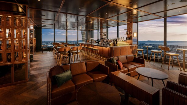 Un bar moderno con techo alto, ventanas amplias y vistas a la ciudad.
