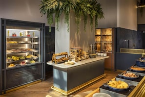 A buffet area with various food items, a central serving station, and a refrigerator with beverages. - Voco Auckland City Centre (Auckland)