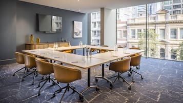 Ein Konferenzraum mit langem Tisch, Stühlen, einem Flachbildfernseher, Kunstwerken und Blick auf Gebäude durch große Fenster.