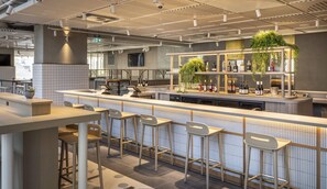 Un espace bar moderne avec un long comptoir, des tabourets de bar et une étagère remplie de bouteilles.