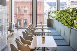 A modern restaurant with a row of booths and tables, large windows with a view of a red brick building, and a green plant wall. - Holiday Inn Express Auckland City Centre (Auckland)