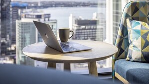 A laptop on a round table with a cup beside it, a sofa with patterned cushions, and a city view through large windows. - Holiday Inn Express Auckland City Centre (Auckland)