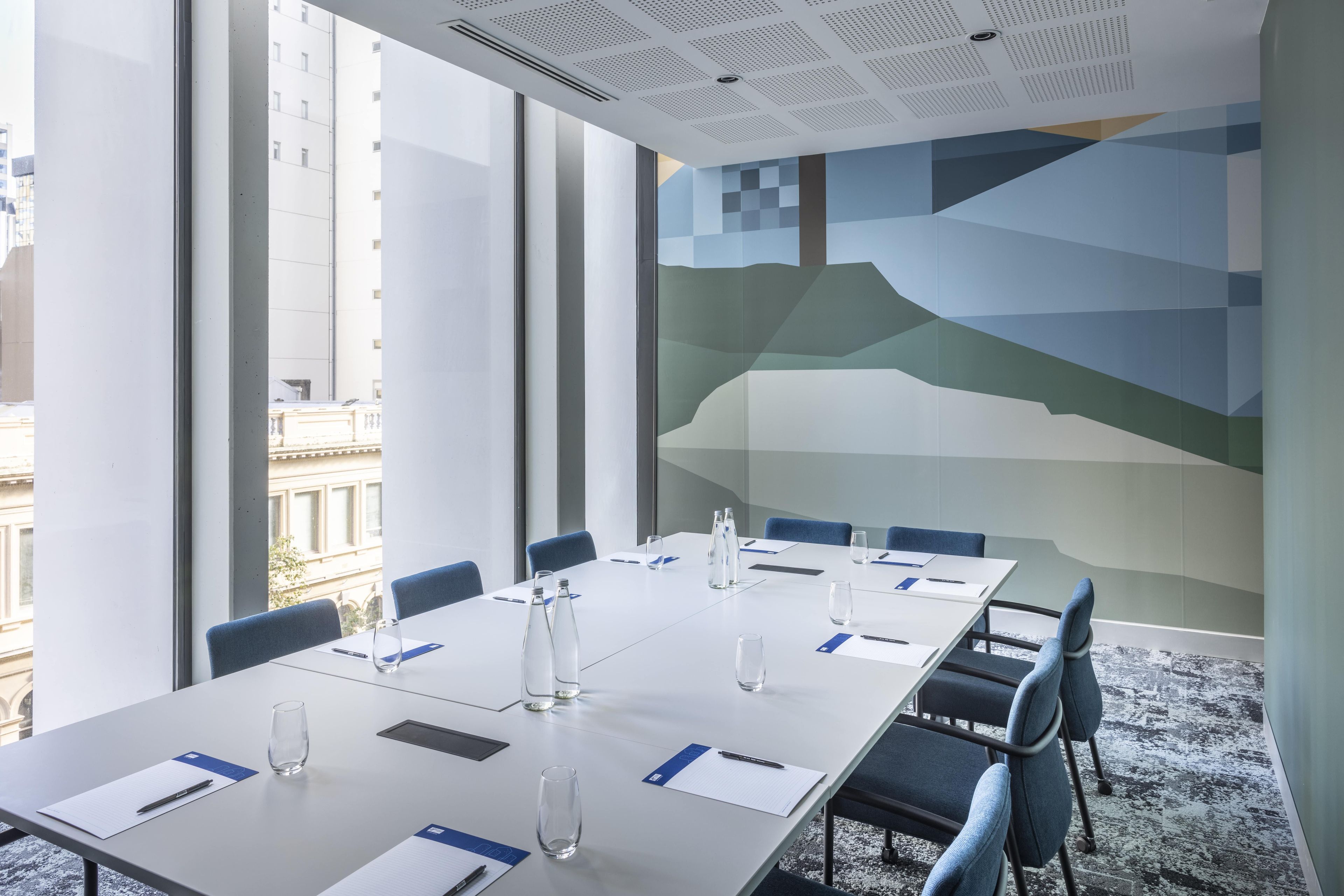 Ein Konferenzraum mit langem Tisch, Stühlen, Wasserflaschen und Papierunterlagen.