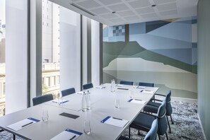 Une salle de conférence avec une longue table, des chaises, des bouteilles d’eau et des documents.