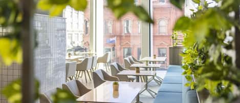 A modern cafe with tables and chairs, large windows, and a view of a red brick building.
