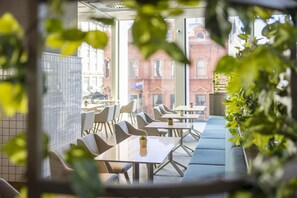 A modern cafe with tables and chairs, large windows, and a view of a red brick building. - Holiday Inn Express Auckland City Centre (Auckland)