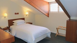 Een slaapkamer met een houten plafond, een bed met wit beddengoed, twee nachtlampjes, een bureau met telefoon en een houten garderobe.