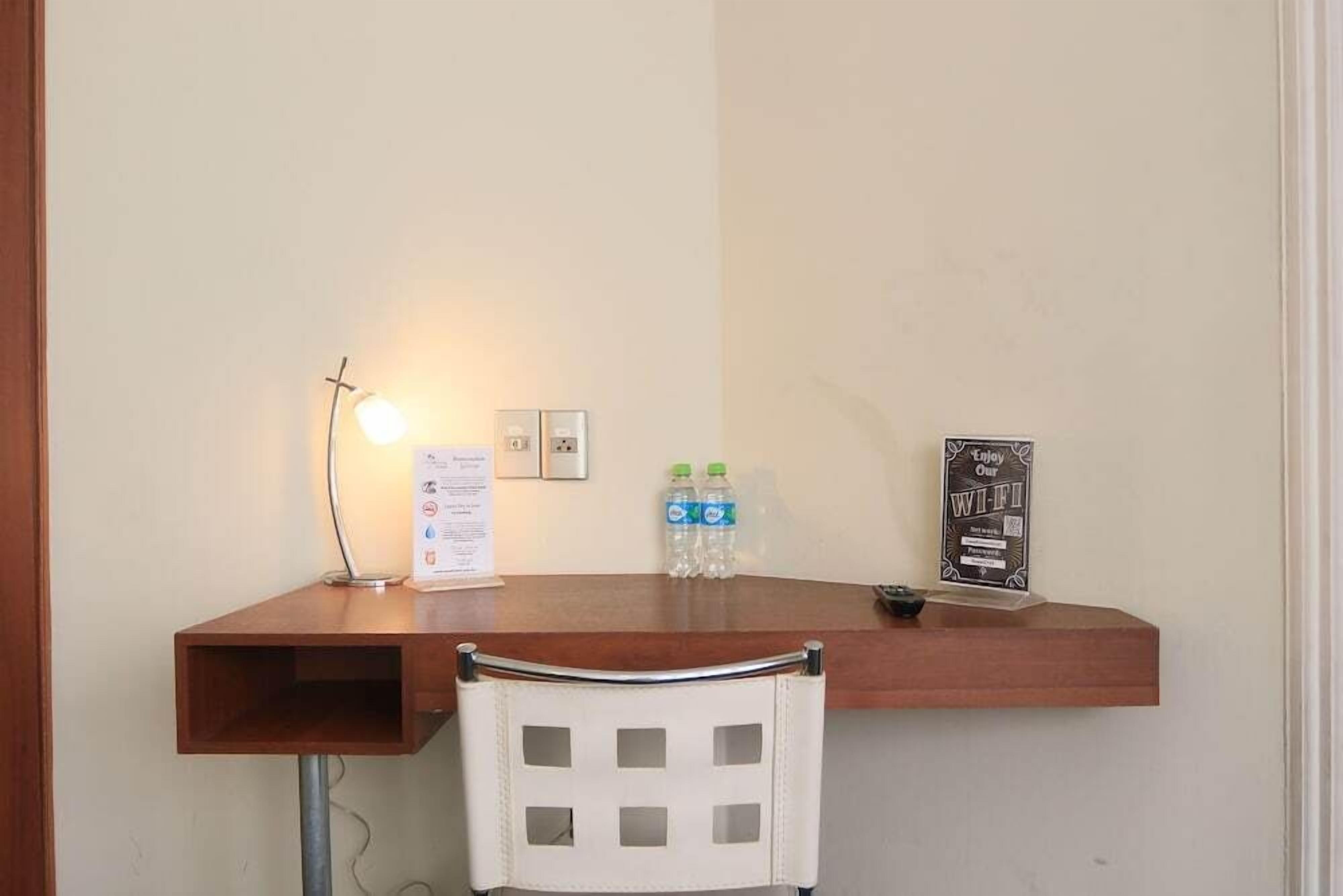 Un pequeño espacio de trabajo con un escritorio, una silla, una lámpara, un letrero y dos botellas de agua.