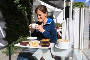 Una persona sentada en una mesa al aire libre con superficie de vidrio, sosteniendo una taza y un plato con postres.