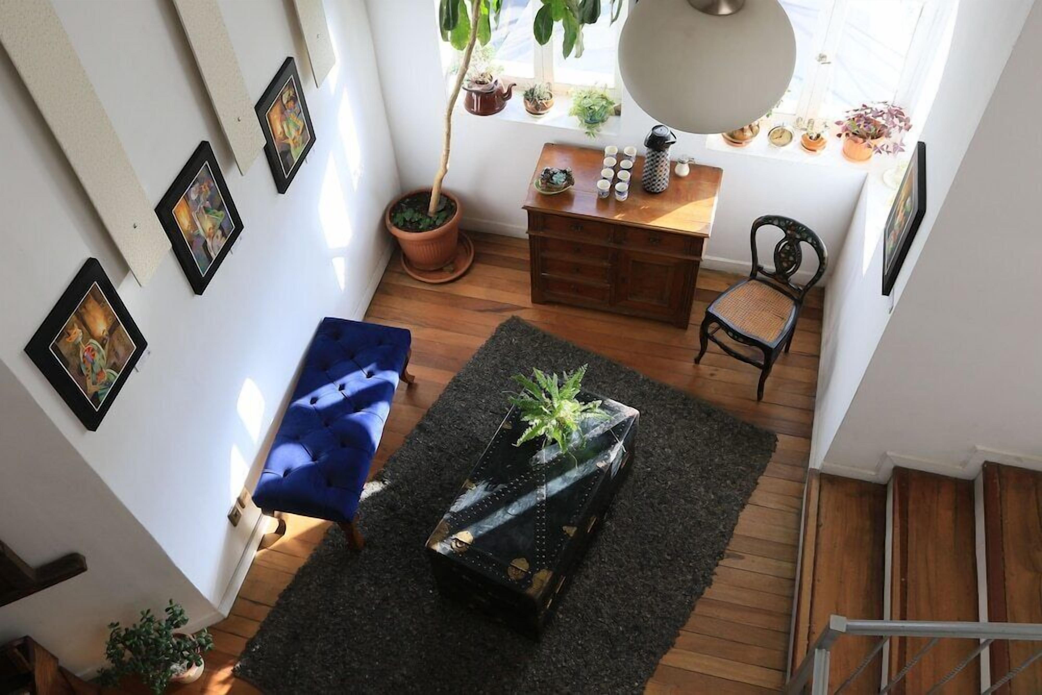Uma sala de estar acolhedora com um sofá azul, uma mesa de centro de madeira com uma planta, e uma escada que leva a outro andar.