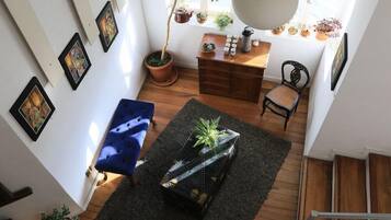 Uma sala de estar acolhedora com um sofá azul, uma mesa de centro de madeira com uma planta, e uma escada que leva a outro andar.