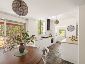 Une cuisine moderne avec des meubles blancs, un sol en pierre et un coin repas comprenant une table et des chaises en bois.