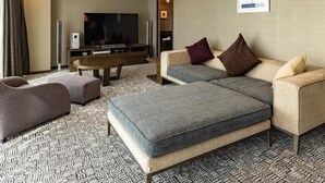 Une chambre d’hôtel moderne équipée d’un téléviseur à écran plat, d’un canapé, d’un pouf et d’un tapis à motifs.