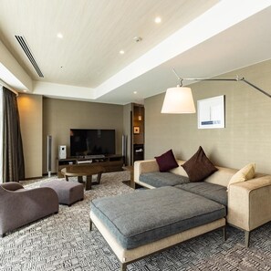 Une chambre d’hôtel moderne équipée d’un téléviseur à écran plat, d’un canapé, d’un pouf et d’un tapis à motifs.