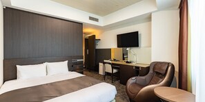 Habitación de hotel con cama, escritorio, silla, televisor y una mesita.