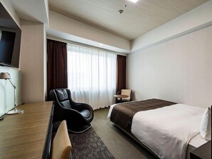 Une chambre d’hôtel avec un lit, un bureau, une chaise, une télévision et une fenêtre avec des rideaux.