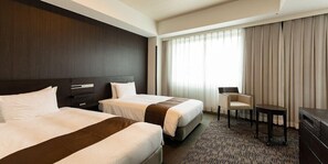Een hotelkamer met twee bedden, een bureau, een stoel en een groot raam met gordijnen.