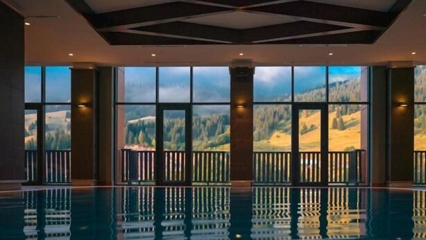 Una piscina interior amplia con ventanas grandes que ofrecen vistas a un paisaje montañoso.