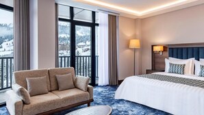 Habitación de hotel con cama, sofá, mesita y ventanas amplias con vista a un paisaje nevado.