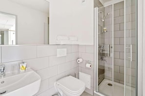 Un baño moderno con lavamanos, inodoro y ducha con mampara de vidrio.