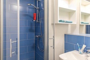 Casa de banho com azulejos azuis, chuveiro com divisória de vidro, lavatório branco e espelho sobre o lavatório.