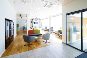 A modern office space with a wooden floor, a central seating area with a colorful sofa, and a glass wall on one side. - Smartments Business Wien Heiligenstadt (Vienna)