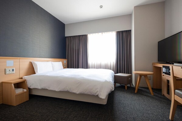 Una habitación de hotel con una cama grande, un escritorio con silla, televisión y ventana con cortinas.