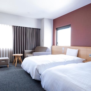 Une chambre d’hôtel avec deux lits, une chaise, une petite table et une fenêtre avec des rideaux.
