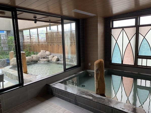 Un'area spa moderna con vasca idromassaggio in vetro, pareti in pietra e vista su un paesaggio naturale.