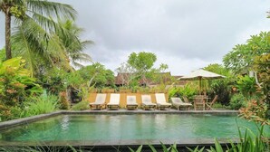 A pool with lounge chairs and an umbrella, surrounded by lush greenery and palm trees. - Bali Sunshine Homestay Ubud by Zuzu (Sukawati)