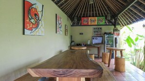 A wooden dining table with benches, surrounded by a thatched roof structure and various artworks on the walls. - Bali Sunshine Homestay Ubud by Zuzu (Sukawati)