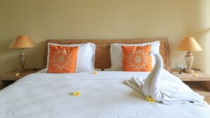 A neatly made bed with white linens, two orange pillows with sun designs, and a white towel with a swan design on a wooden headboard. - Bali Sunshine Homestay Ubud by Zuzu (Sukawati)