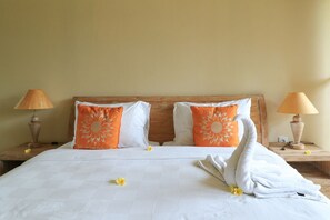 A neatly made bed with white linens, two orange pillows with sun designs, and a white towel with a swan design on a wooden headboard. - Bali Sunshine Homestay Ubud by Zuzu (Sukawati)