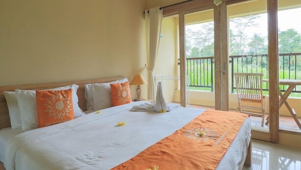 A hotel room with a bed, a balcony, and a view of greenery. - Bali Sunshine Homestay Ubud by Zuzu (Sukawati)