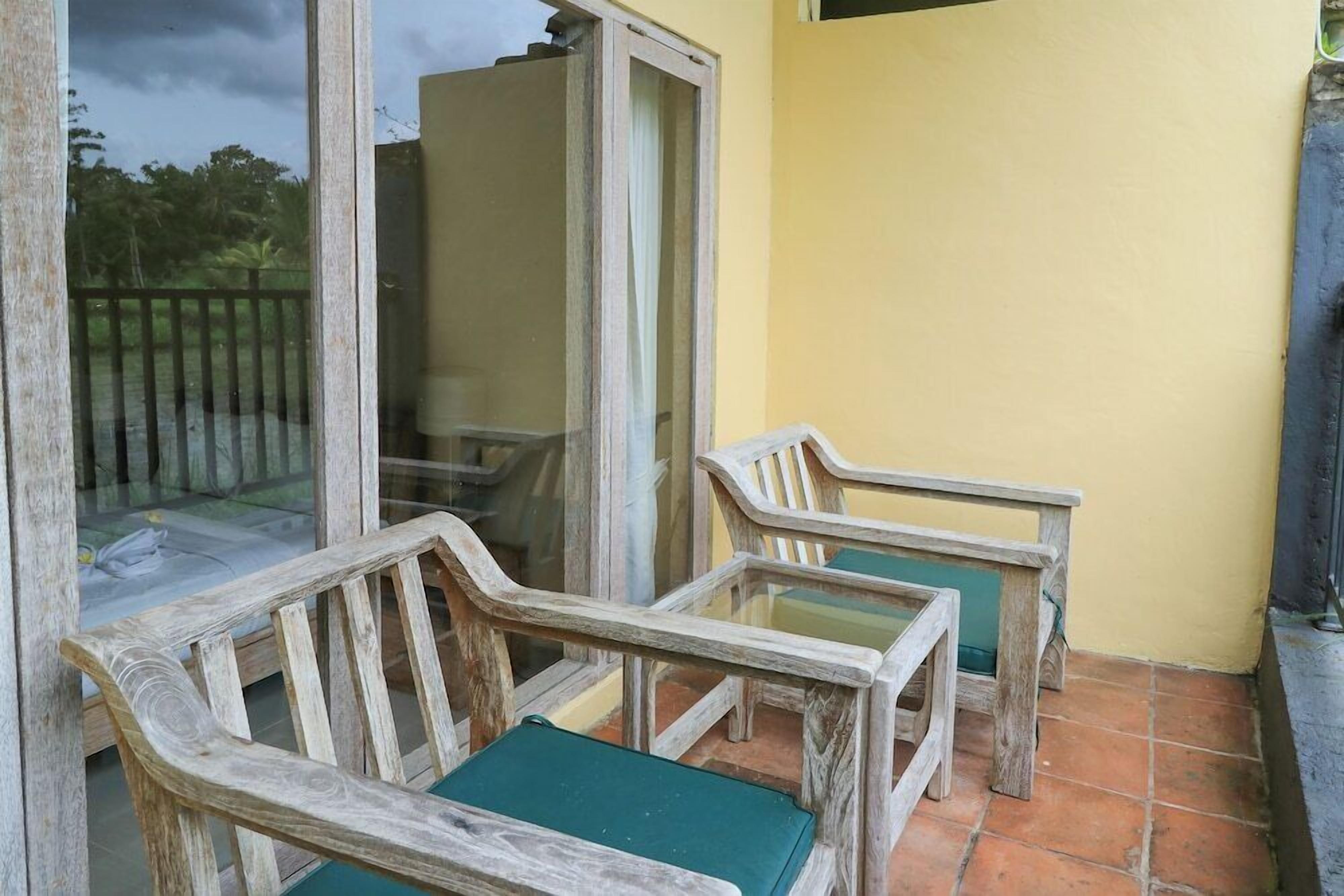 A balcony with two wooden chairs and a table, a glass door, and a yellow wall.