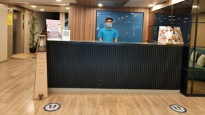 A reception desk with a man standing behind it, a potted plant to the left, and a Buddha statue on the right. - Kanak Beacon Hotel, Ahmedabad (Ahmedabad)