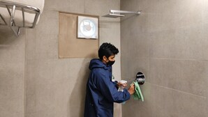 A person cleaning a shower area in a bathroom with tiled walls and a showerhead mounted on the wall.
