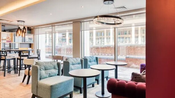 A modern lounge area with seating and tables, large windows offering a view of the cityscape. - Premier Inn Banbury Town Centre Hotel (Banbury)