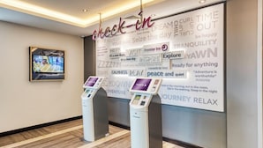A hotel reception area with a check-in kiosk and a wall displaying motivational phrases and the Premier Inn logo. - Premier Inn Banbury Town Centre Hotel (Banbury)