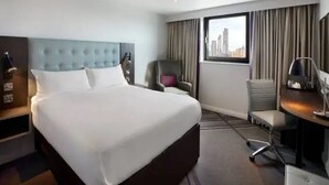 A hotel room with a large bed, a desk with a chair, a chair, a window with a city view, and a headboard. - Premier Inn Banbury Town Centre Hotel (Banbury)