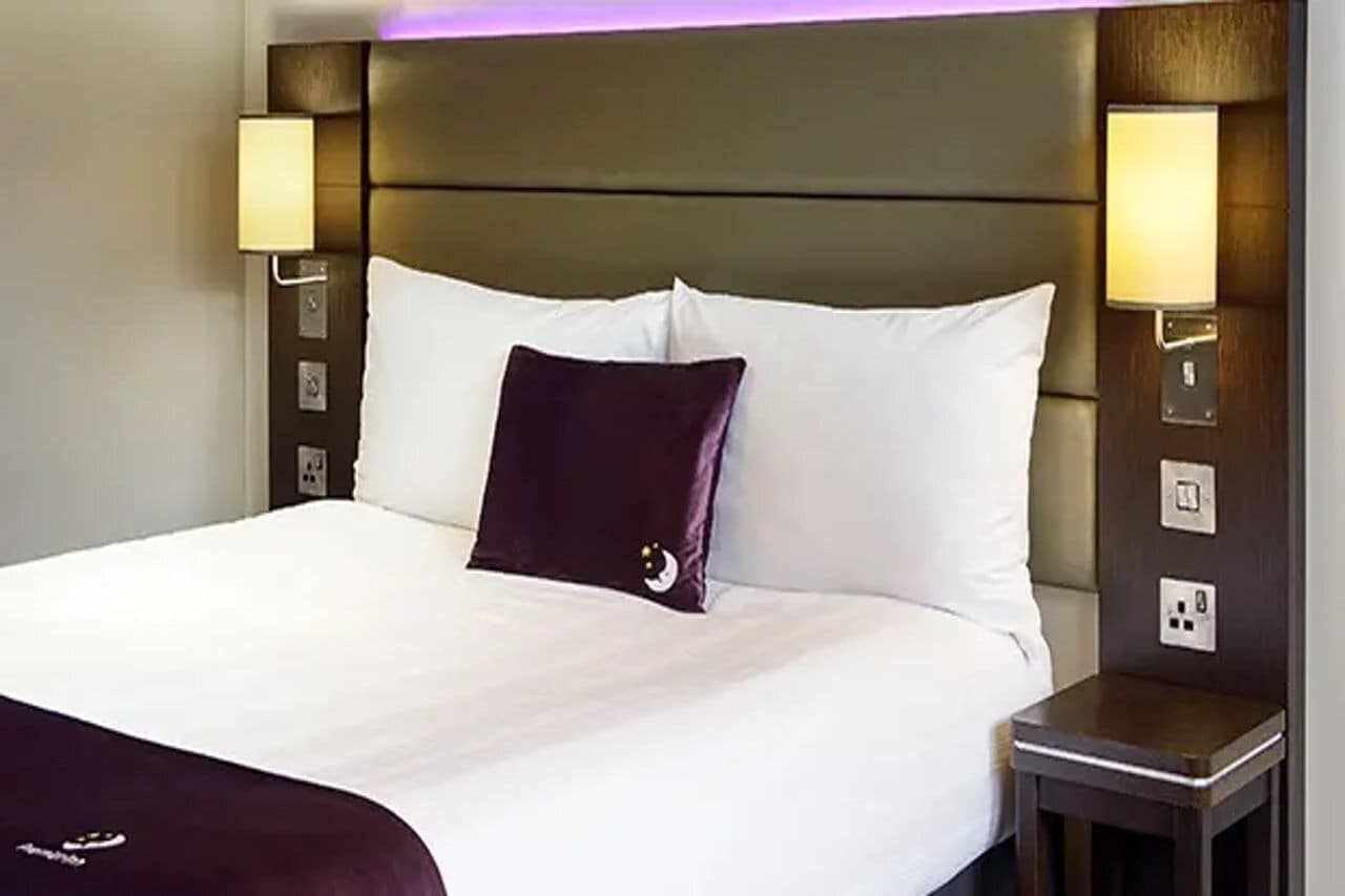 Una habitación de hotel con una cama grande, dos lámparas de noche y una mesita de noche.