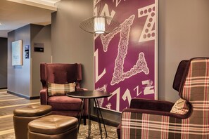 A hotel lobby with a red armchair, a plaid armchair, a small table, and a wall with a large decorative pattern. - Premier Inn Edinburgh City Centre Hotel (Edinburgh)