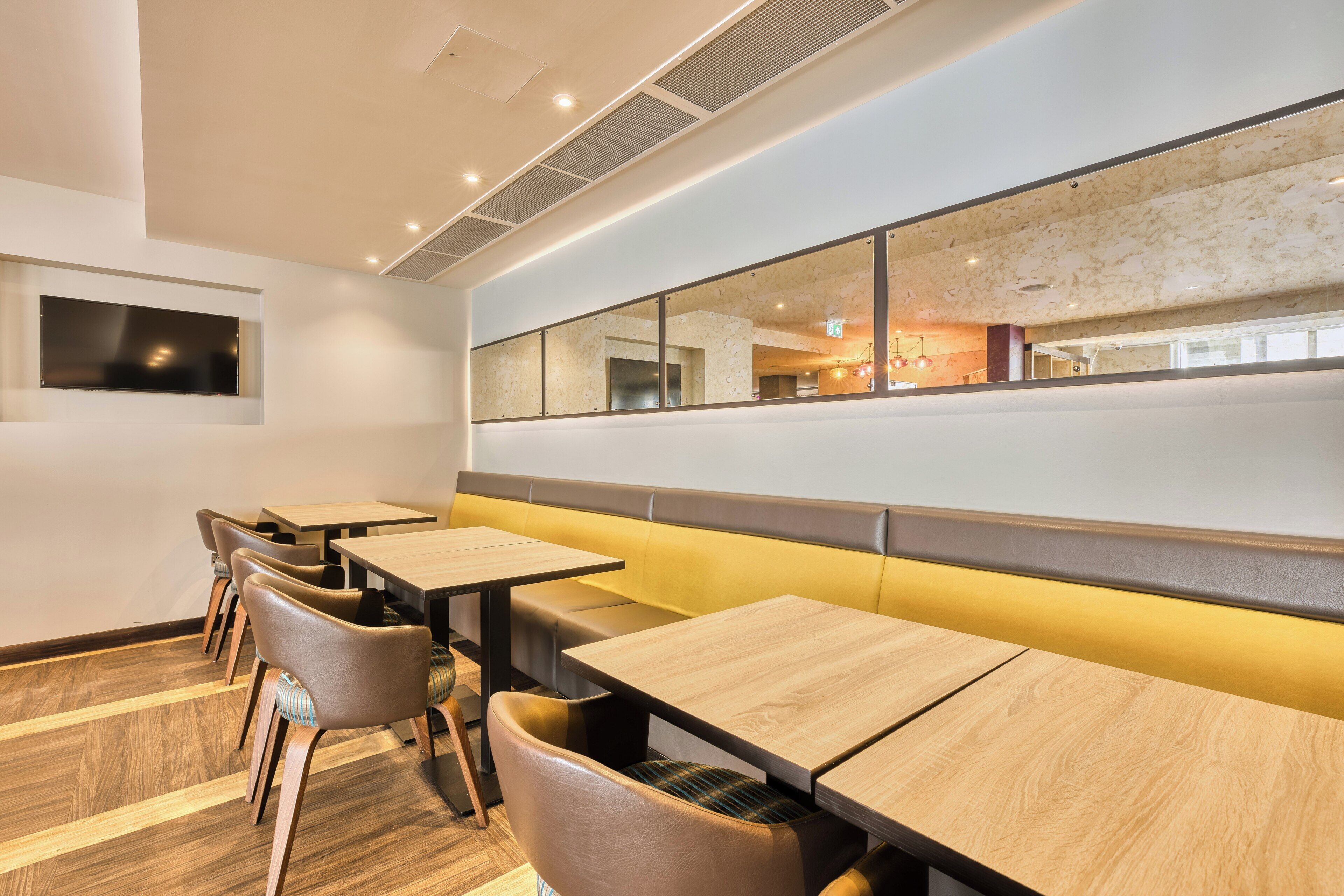 A modern dining area with wooden tables and chairs, a large mirror, and a view of the restaurant's interior.