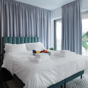 A hotel room with a large bed, grey curtains, and a view of the city. - Liv Urban Larnaca (Larnaca)
